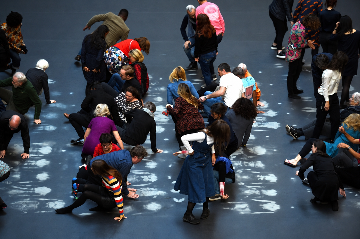 Persone accovacciate e sedute sul pavimento termosensibile della Turbine Hall della Tate Modern, che lasciano pallide impronte delle mani nei punti in cui il calore del loro corpo ne ha modificato il colore